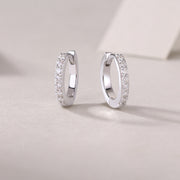 A pair of silver hoop earrings with round-cut moissanite stones set in a pavé pattern on a white surface.